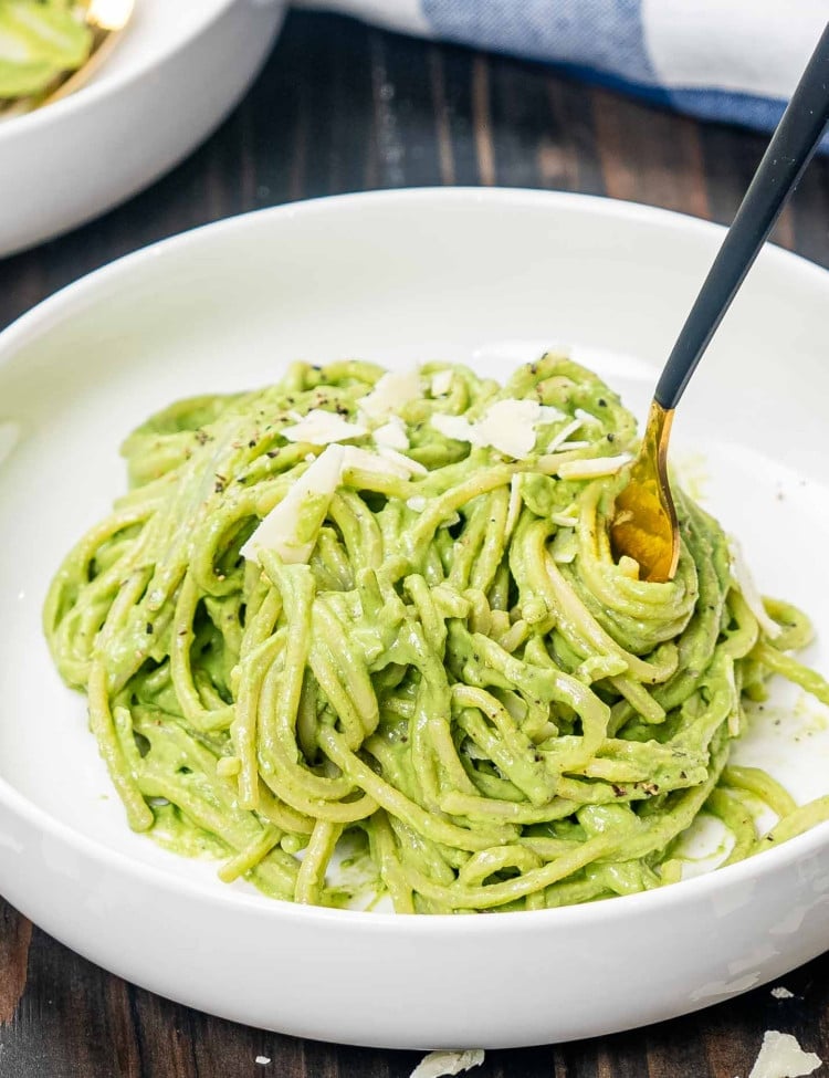 a white bowl with a serving of creamy avocado spinach pasta garnished with parmesan.