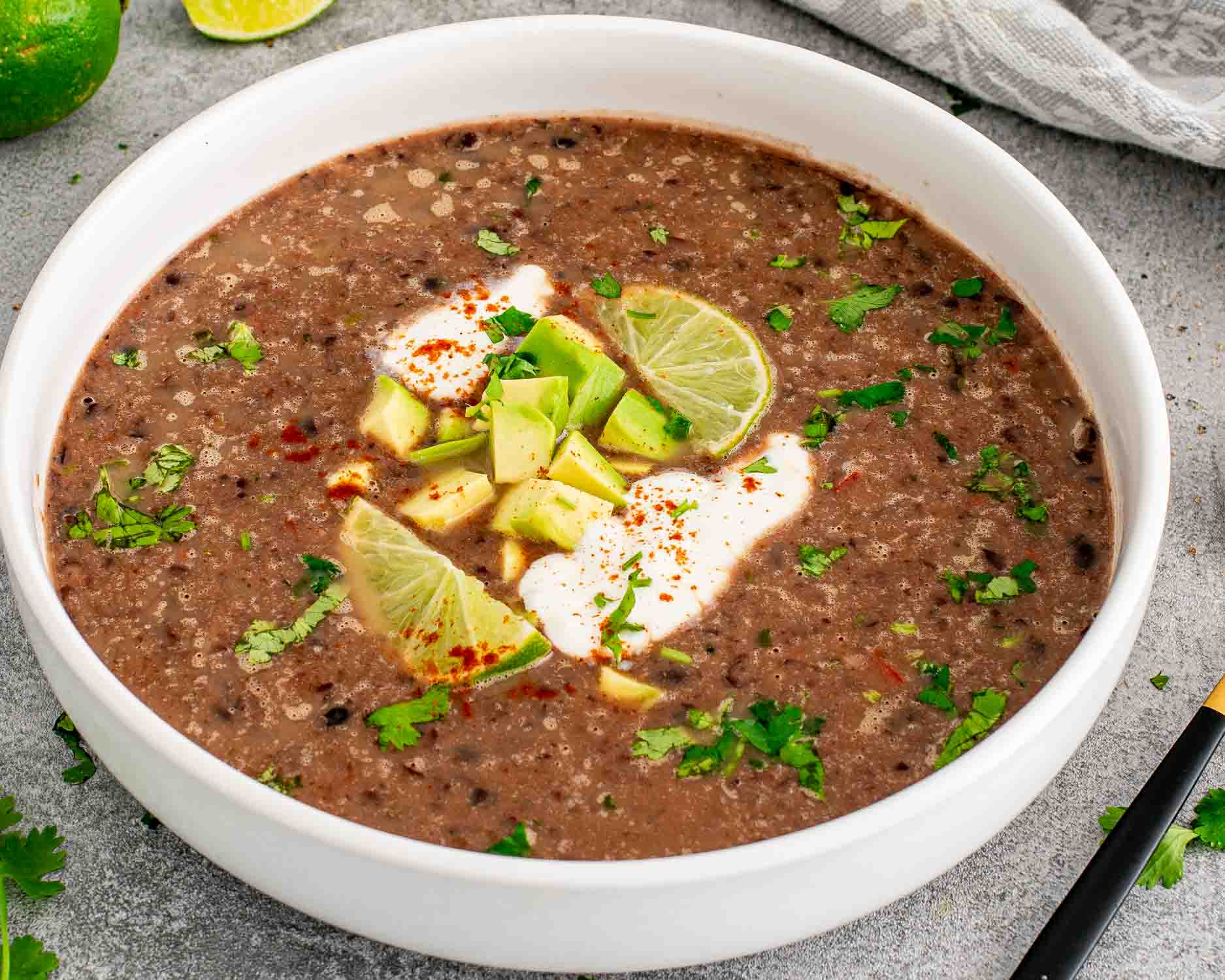 a serving of black bean soup garnished with a dollop of sour cream, cilantro and lime wedges.