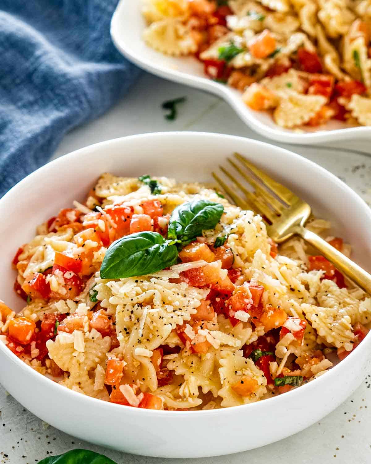 bruschetta pasta in a white bowl with a golden fork.