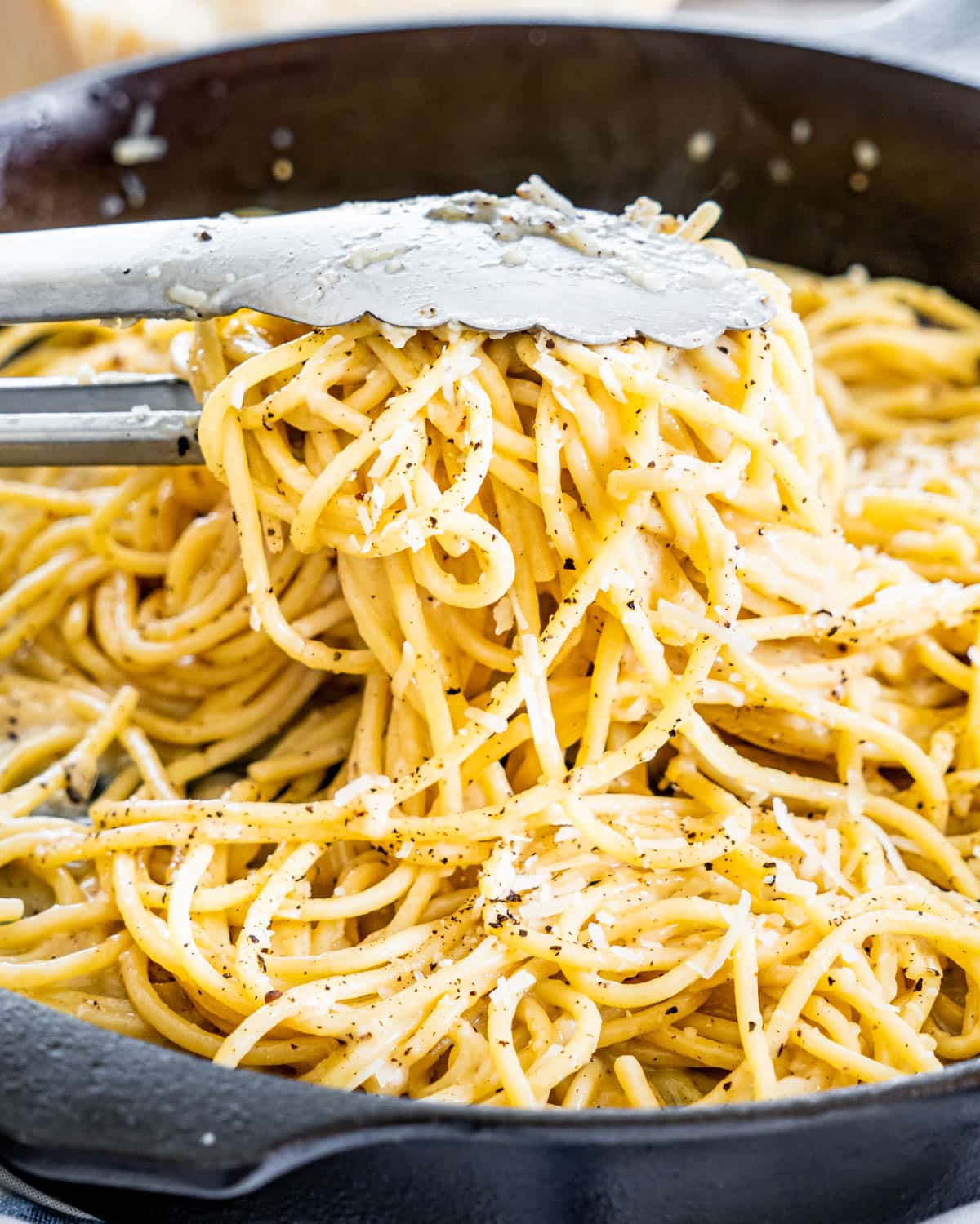 tongs pulling out some pasta from a skillet