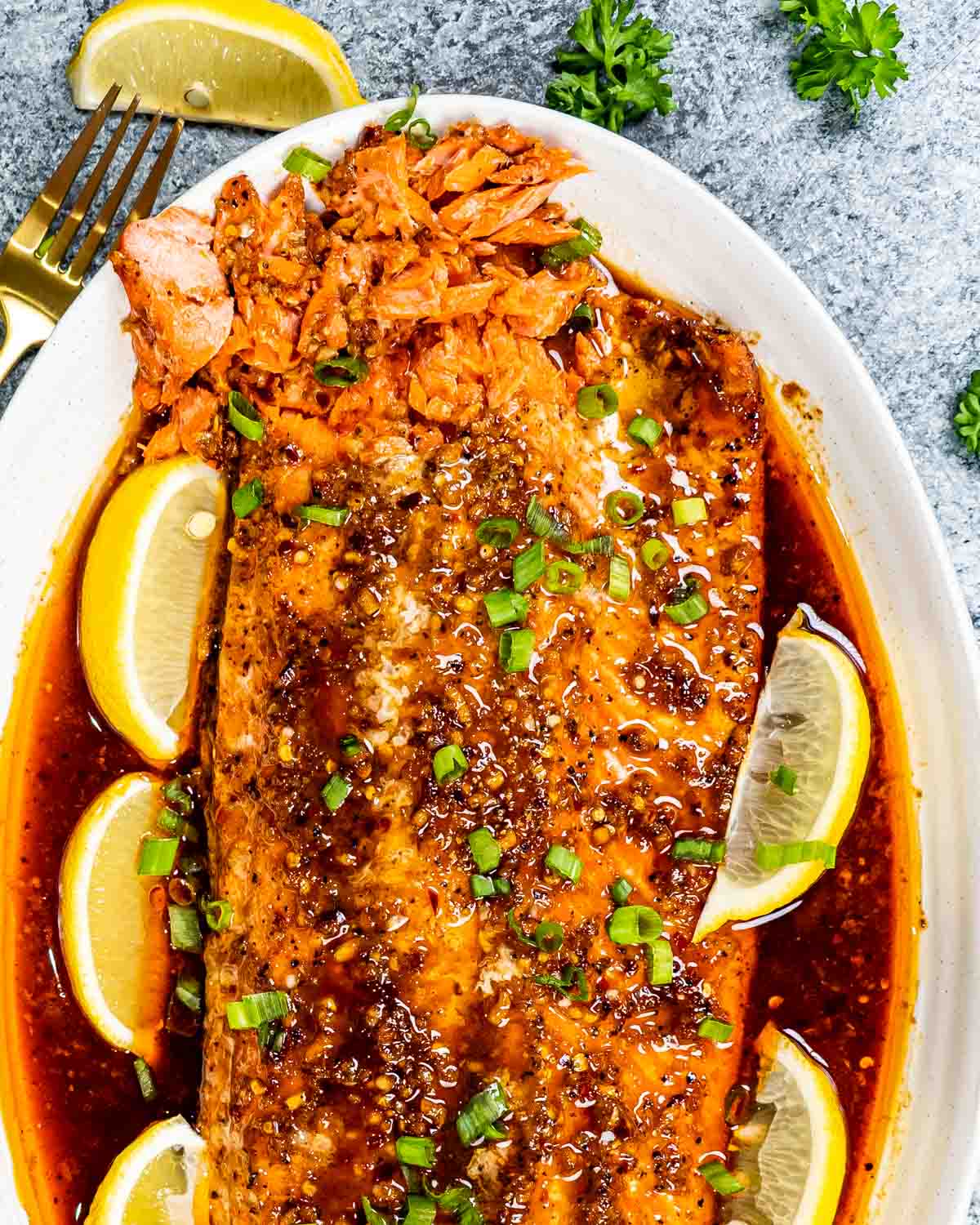 firecracker salmon on a serving platter garnished with lemon wedges and green onions.
