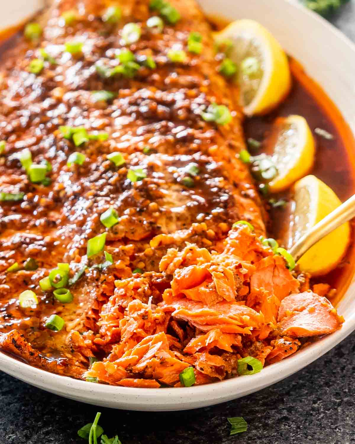 firecracker salmon on a serving platter garnished with lemon wedges and green onions.