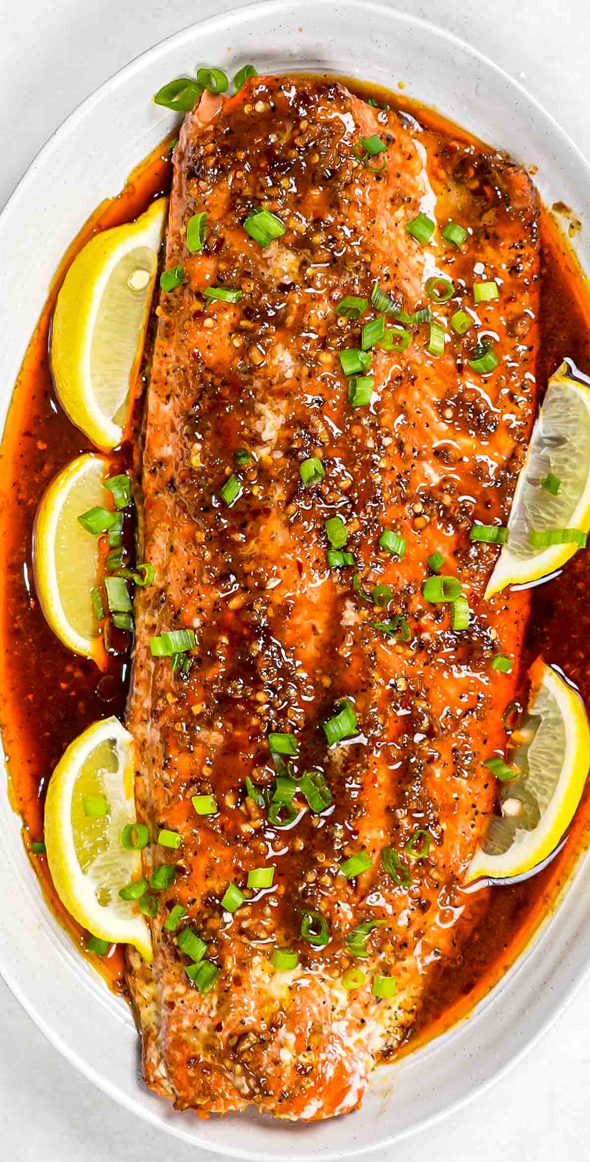 firecracker salmon on a serving platter garnished with lemon wedges and green onions.