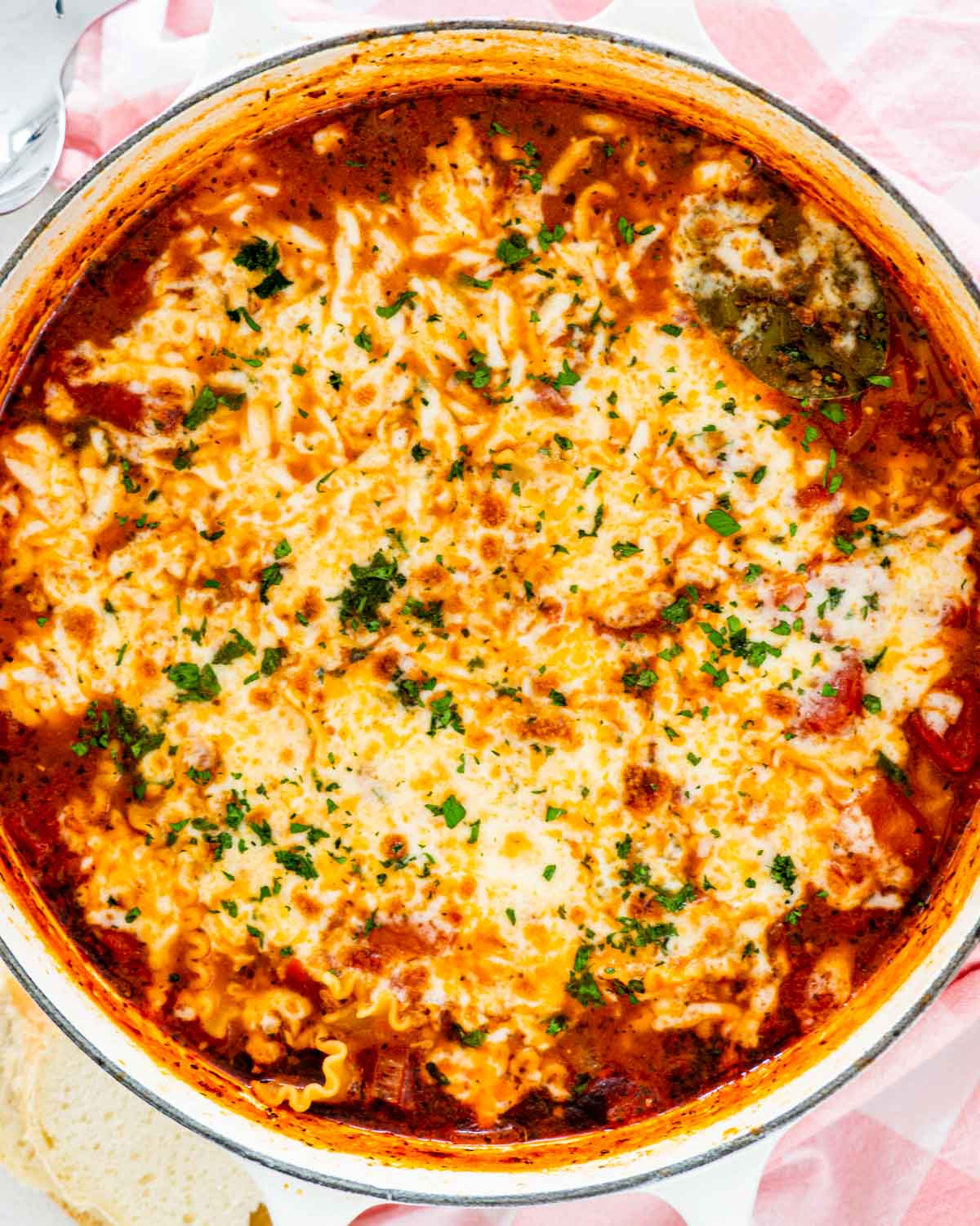 freshly made lasagna soup topped with cheese in a dutch oven and garnished with parsley.