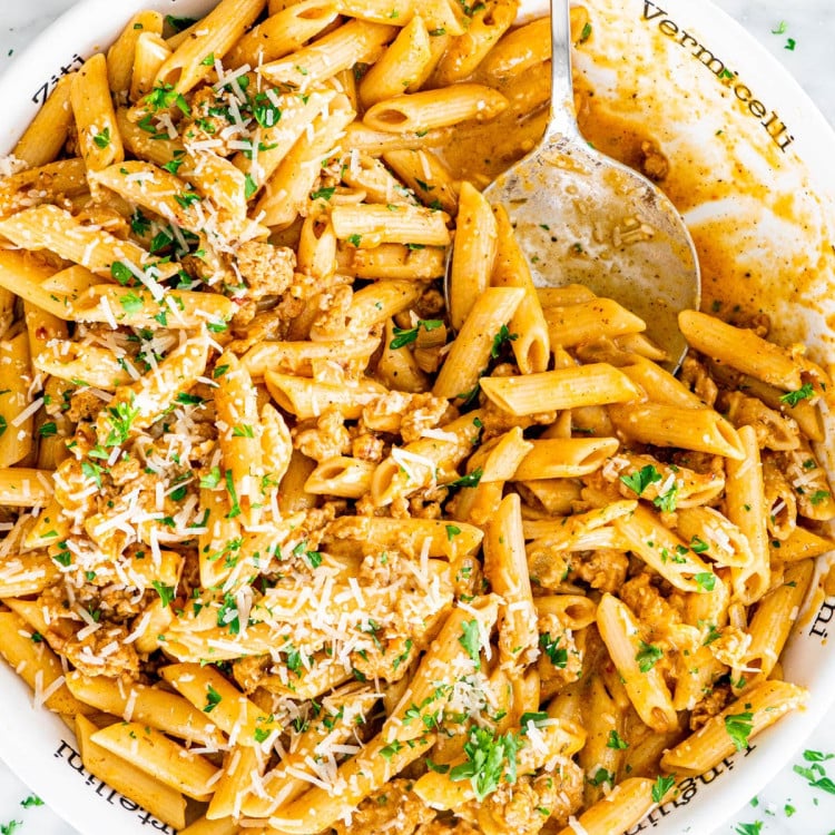 overhead shot of pumpkin sausage pasta in a large serving bowl with a serving spoon taking a scoop