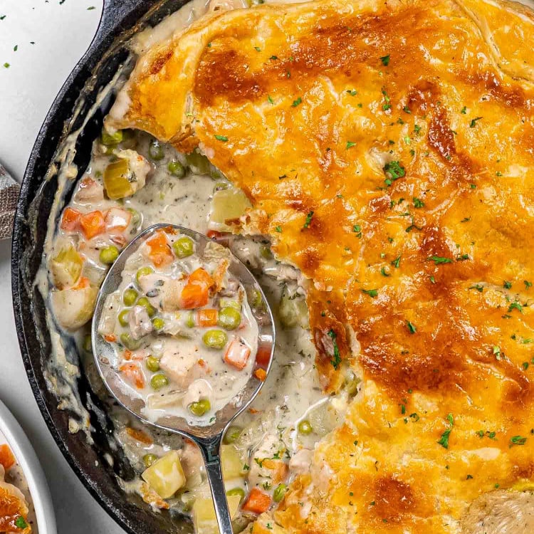 skillet chicken pot pie in a cast iron skillet with a serving taken out.