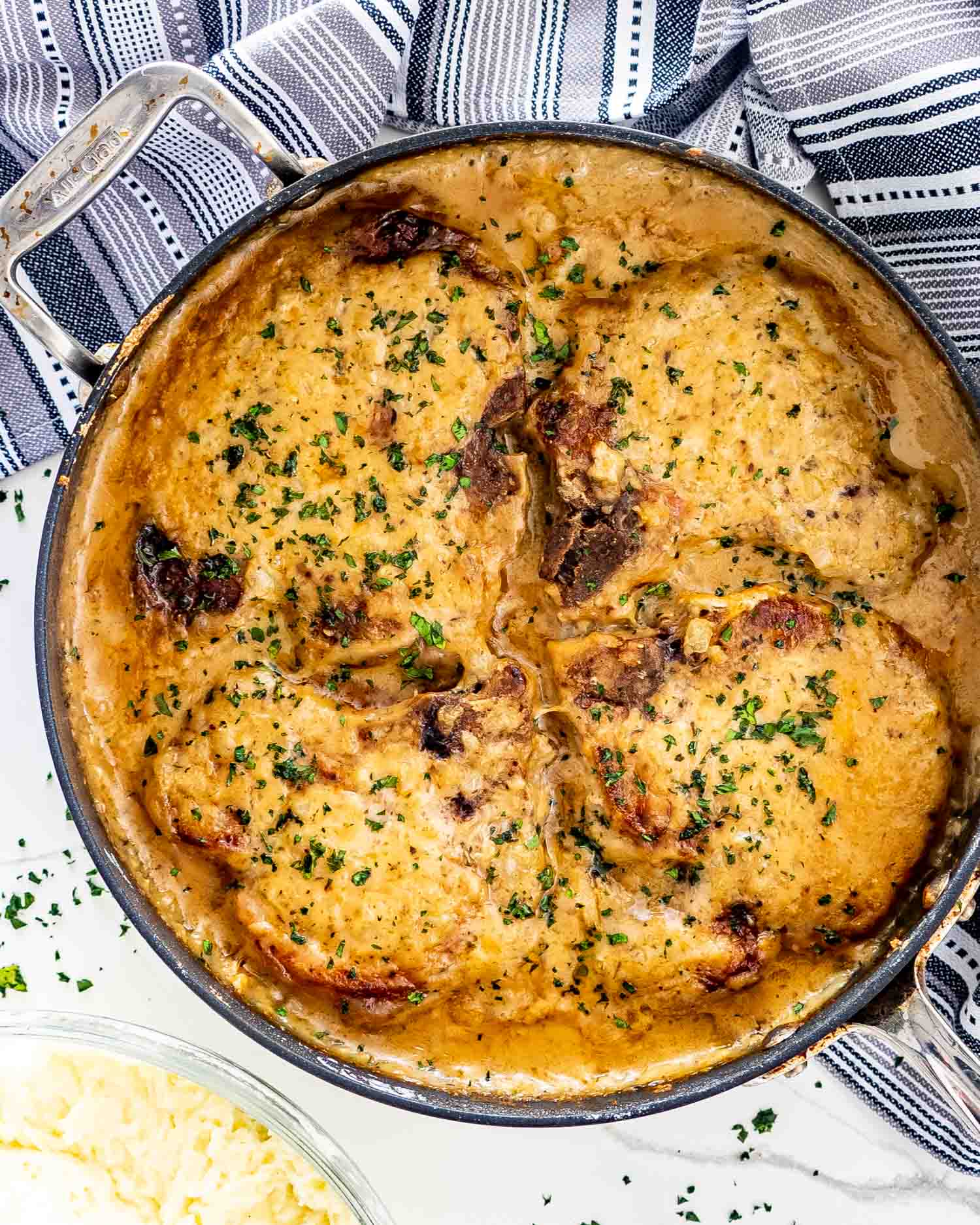 smothered pork chops in a skillet garnished with parsley.