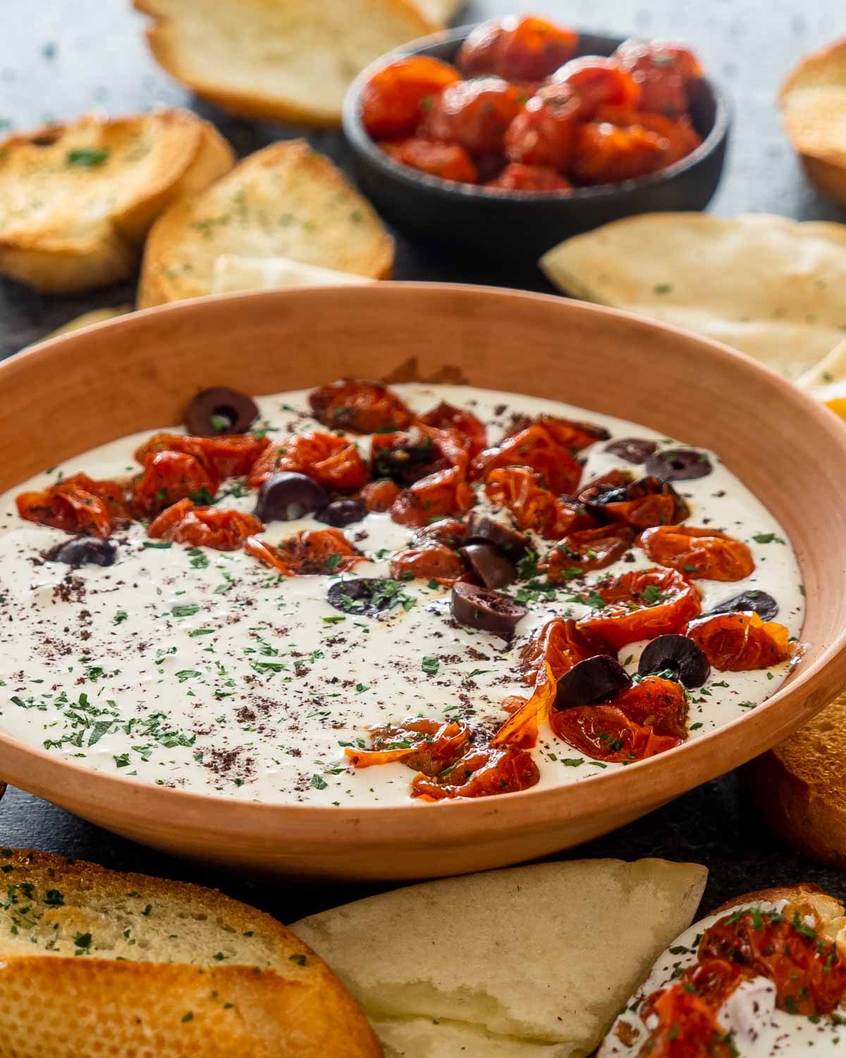 a bowl with whipped feta dip topped with roasted tomatoes surround by pita chips.