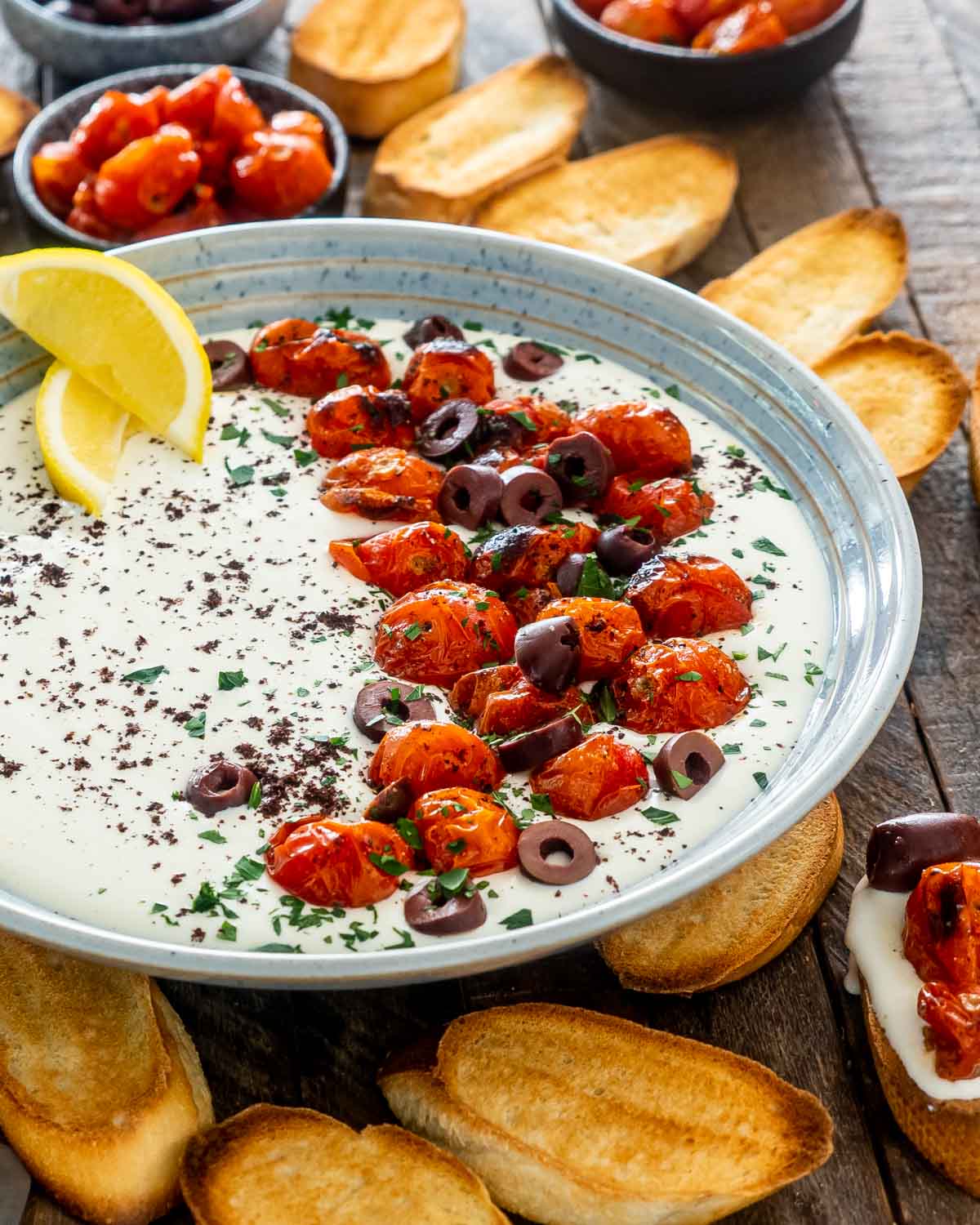 a bowl with whipped feta dip topped with roasted tomatoes surround by pita chips.